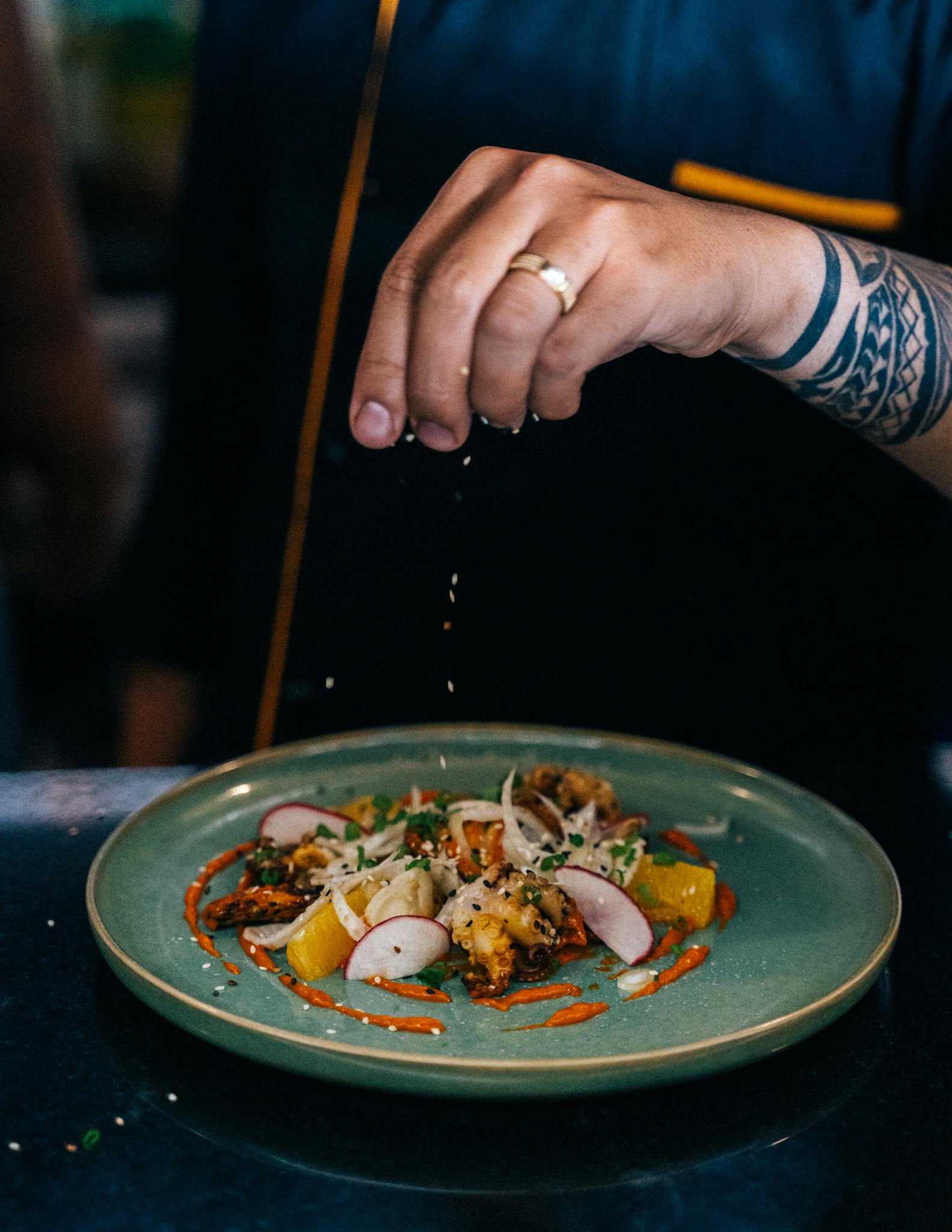 A chef adding final touches to a gourmet dish in an indoor restaurant kitchen.
