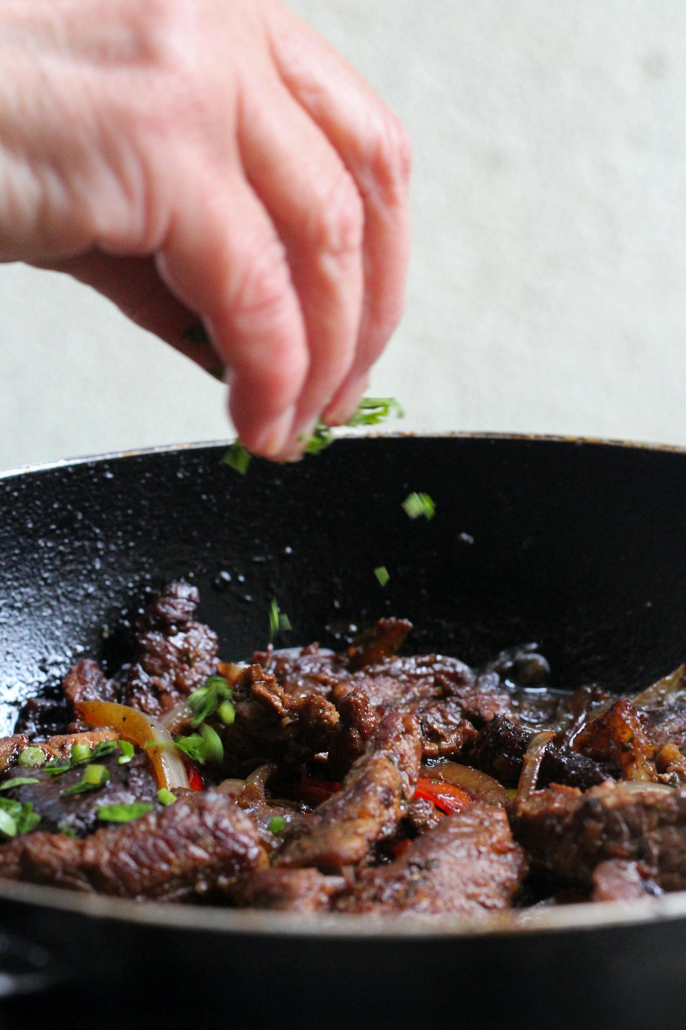 Close-up of a chef's hand garnishing stir-fried beef with fresh herbs in a pan.